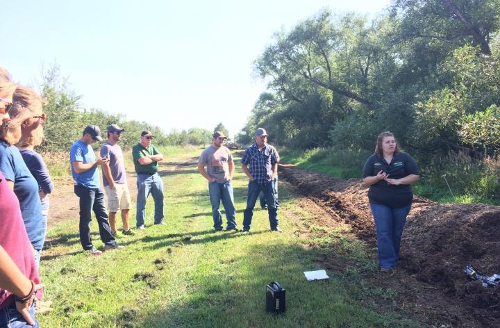 woman standing next to manure compost pile talking to a crowdabout