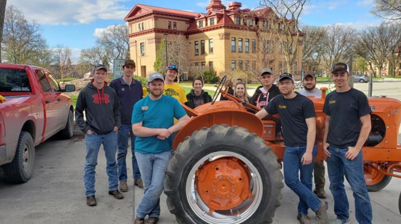 students posing with a red tractor